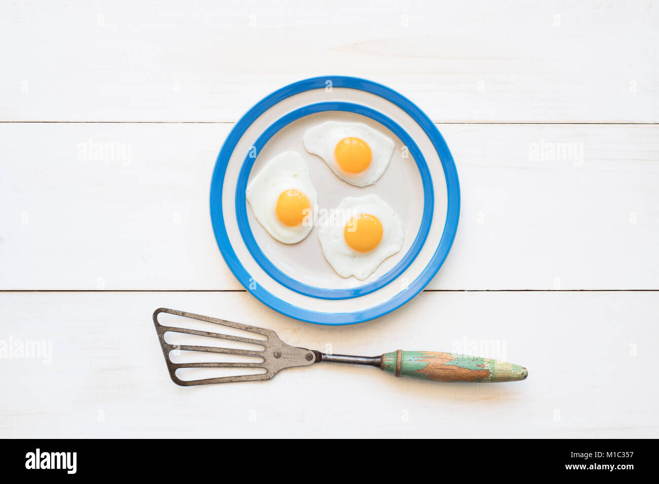 Fried Quail Eggs on a cornishware plate with a vintage spatula from above Stock Photo