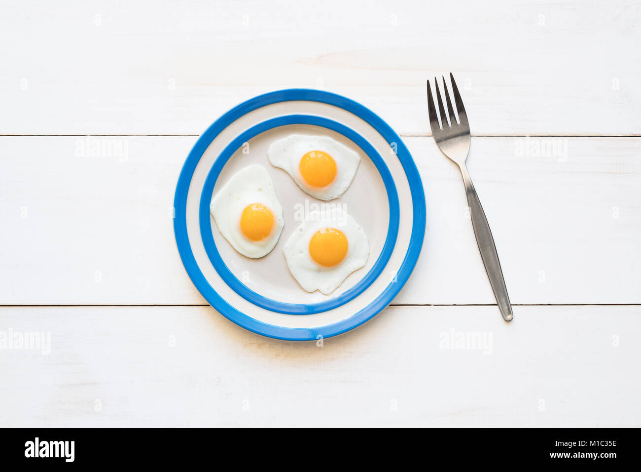 Fried Quail Eggs on a cornishware plate with a fork from above Stock Photo