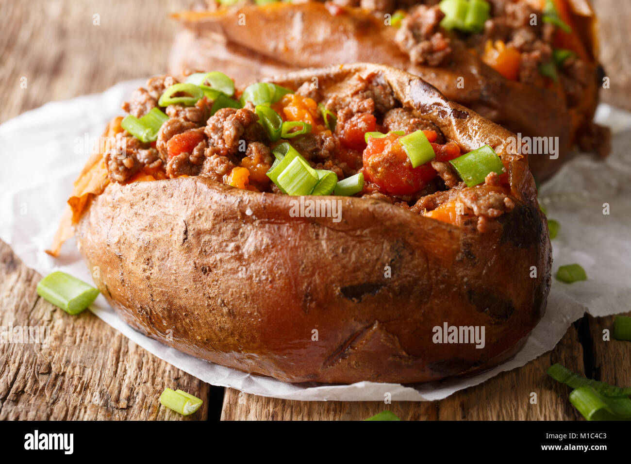 Baked sweet potatoes stuffed with ground beef with tomatoes and onions macro on paper on a table