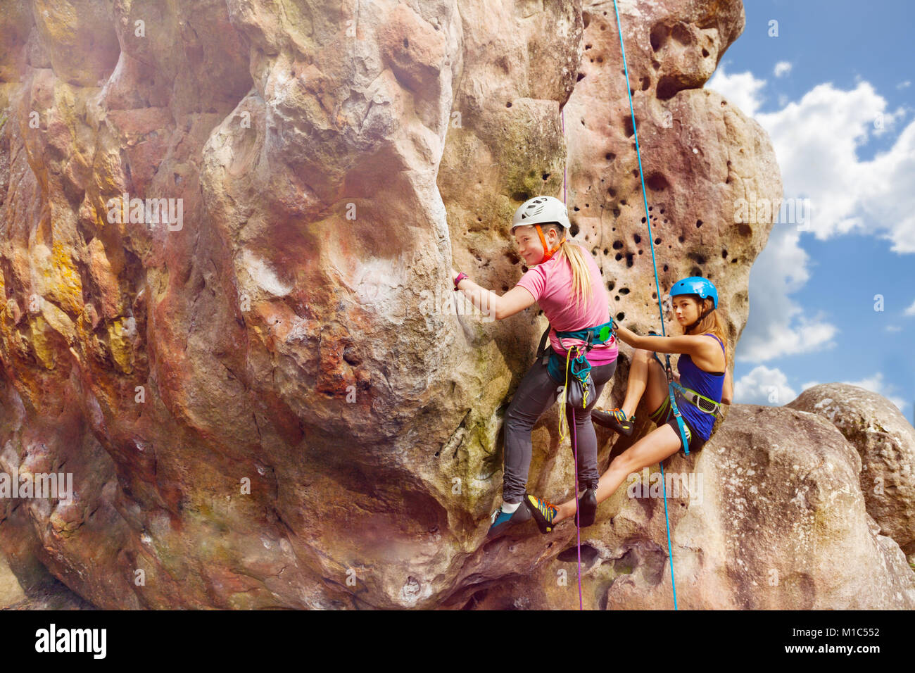 Female alpinists in helmets climbs the rock with harnesses against cloudy sky Stock Photo