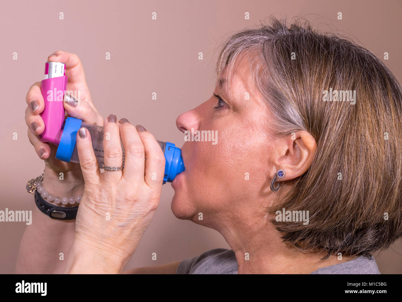 A caucasian woman in her fifties, using an AeroChamber Plus inhaler / puffer to deliver a metered dose of asthma medication in aerosol form. UK. Stock Photo