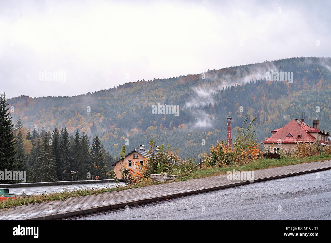 Fog and mist over the pine mountain forest with traditional old village houses and the road Stock Photo