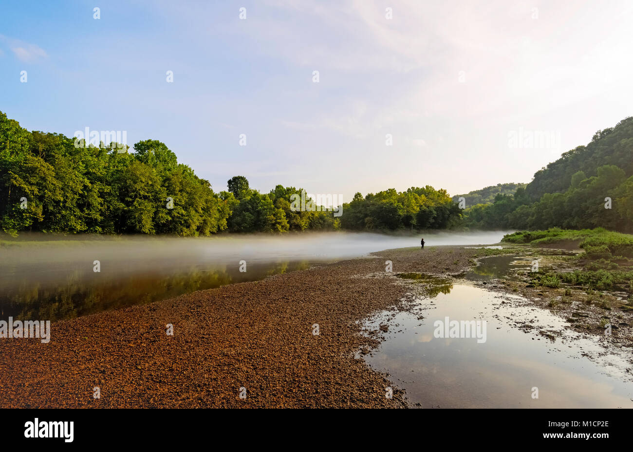 Morning mist lifts over the Little Tennessee river flanked by trees and stony bank near Gatlinburg, Tennessee, USA. Stock Photo