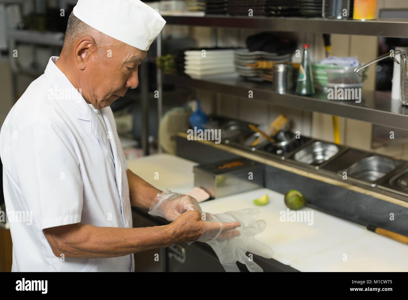 Senior chef wearing plastic gloves in kitchen Stock Photo