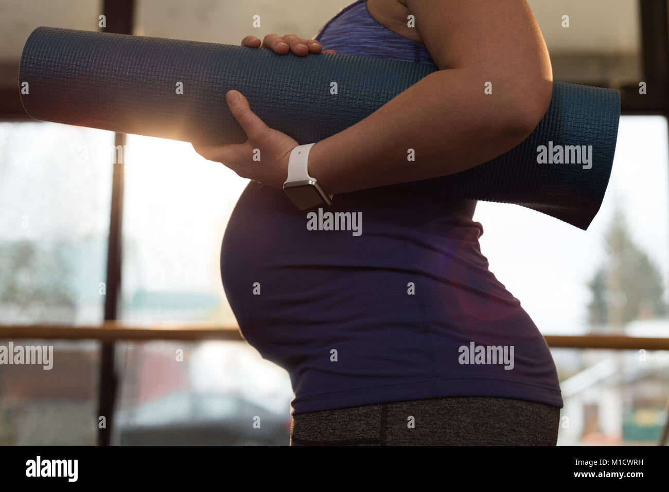 Pregnant woman holding exercise mat at home Stock Photo