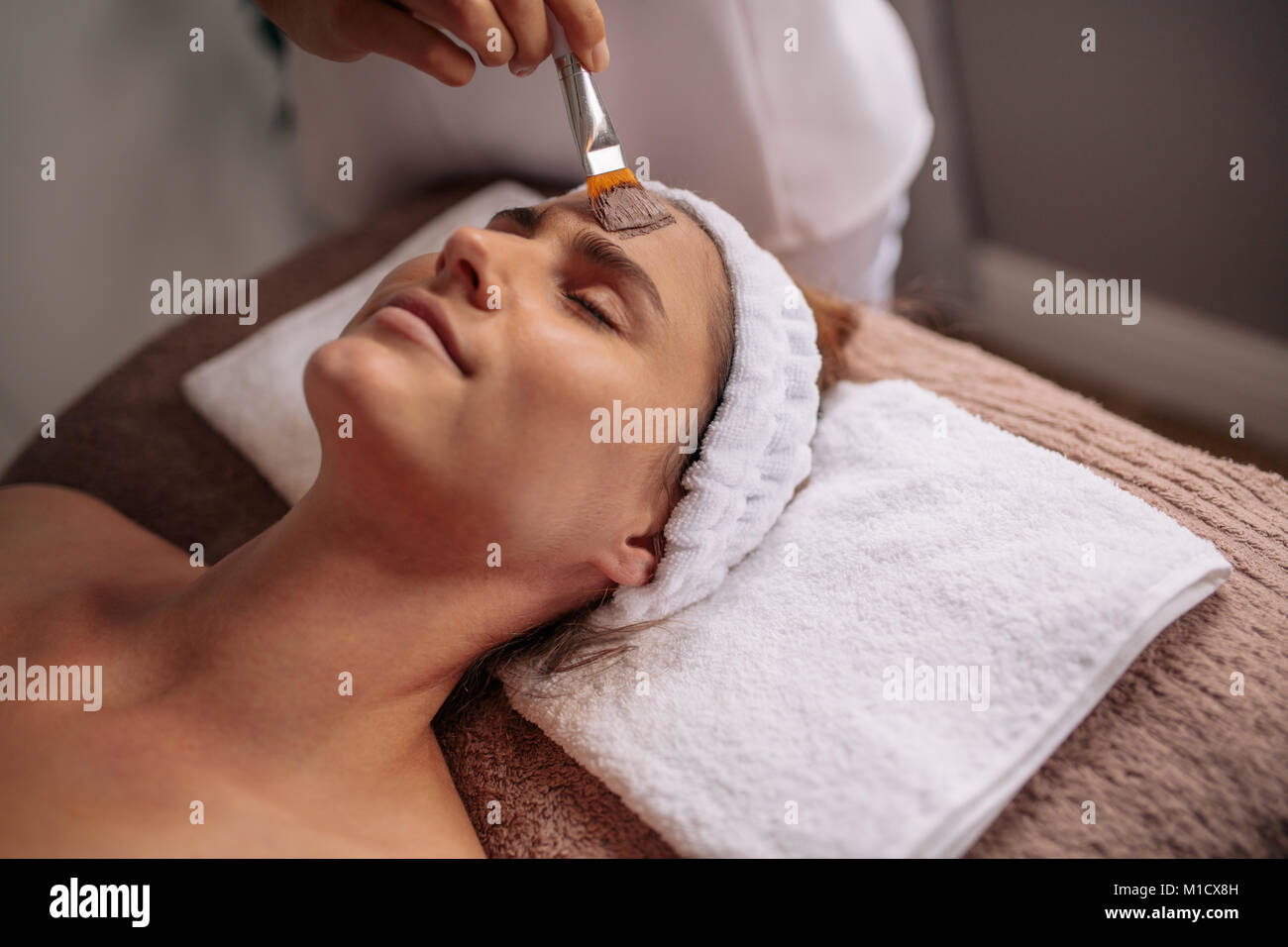 Woman getting facial nourishing mask by beautician at spa salon. Caucasian female receiving a face mask treatment in a beauty center by therapist. Stock Photo