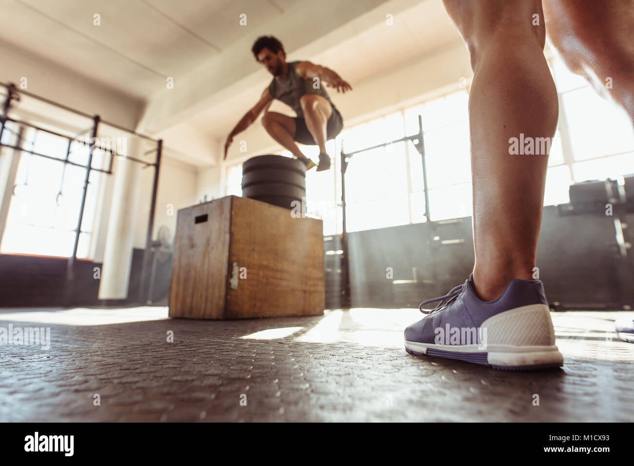 Fit young man box jumping at a cross training style gym. Male athlete performing box jumps at health club. Stock Photo