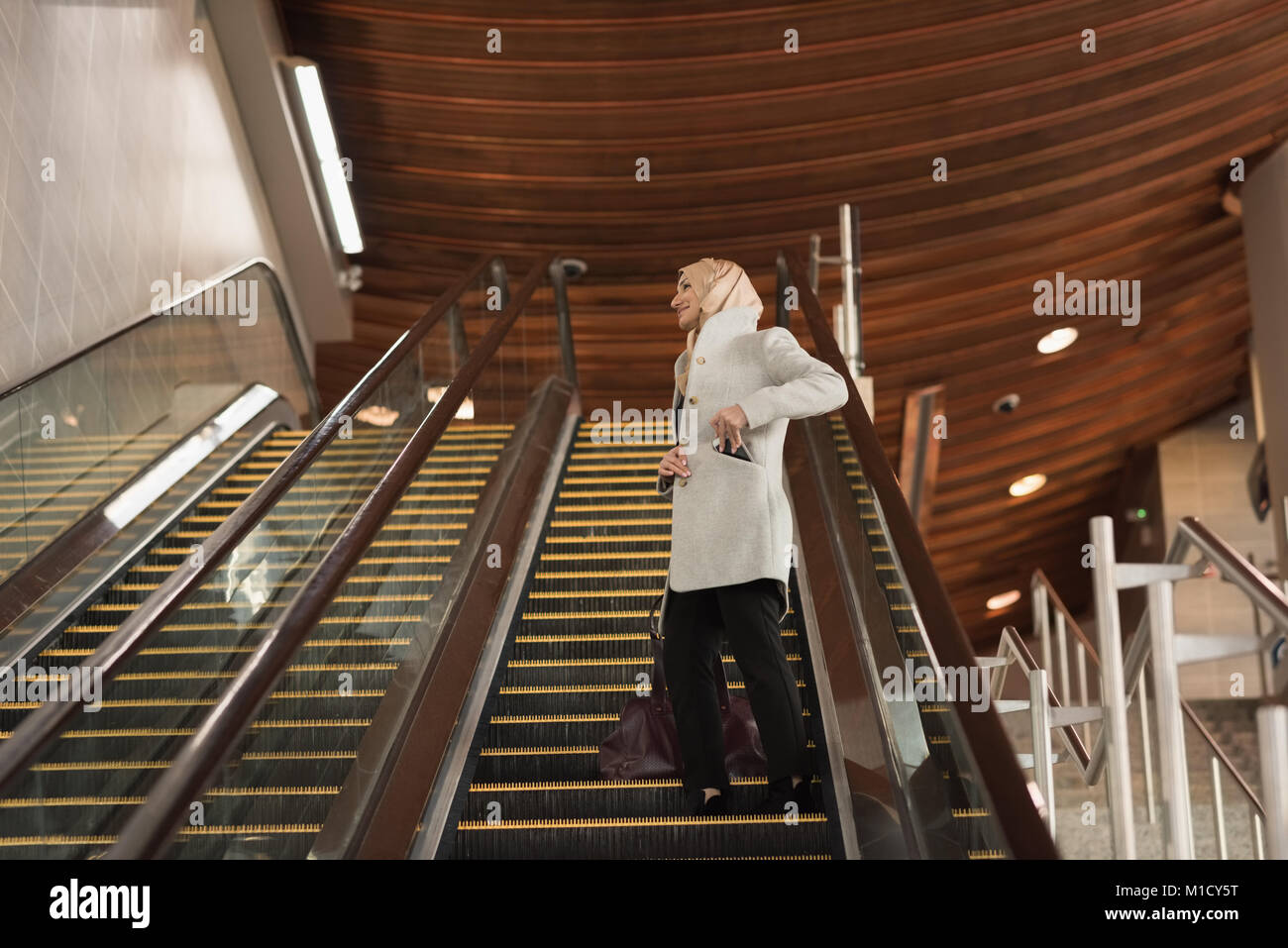 Woman in hijab moving down from escalator Stock Photo