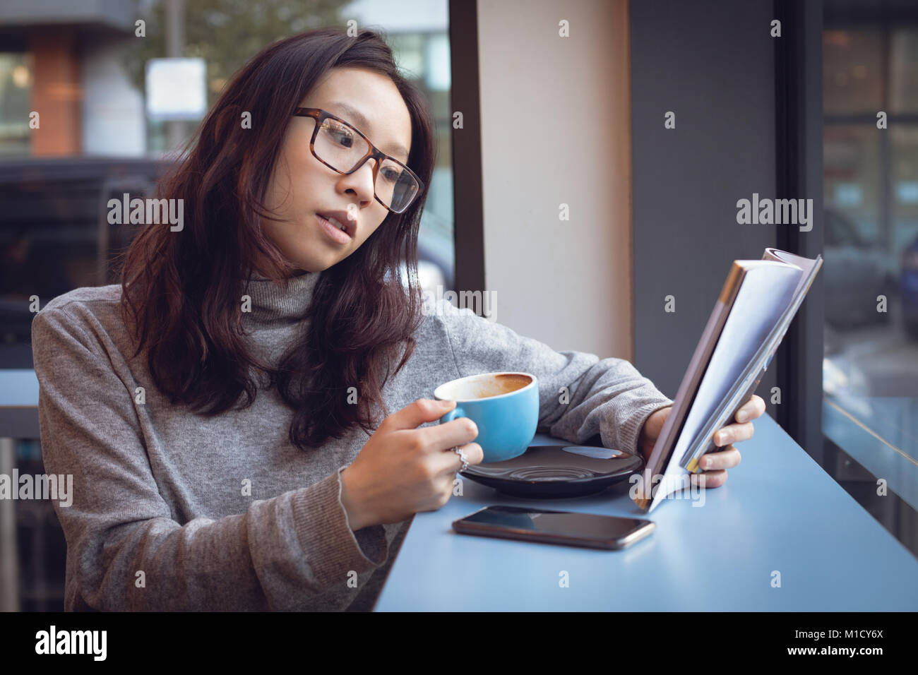 Beautiful woman reading magazine while having coffee Stock Photo