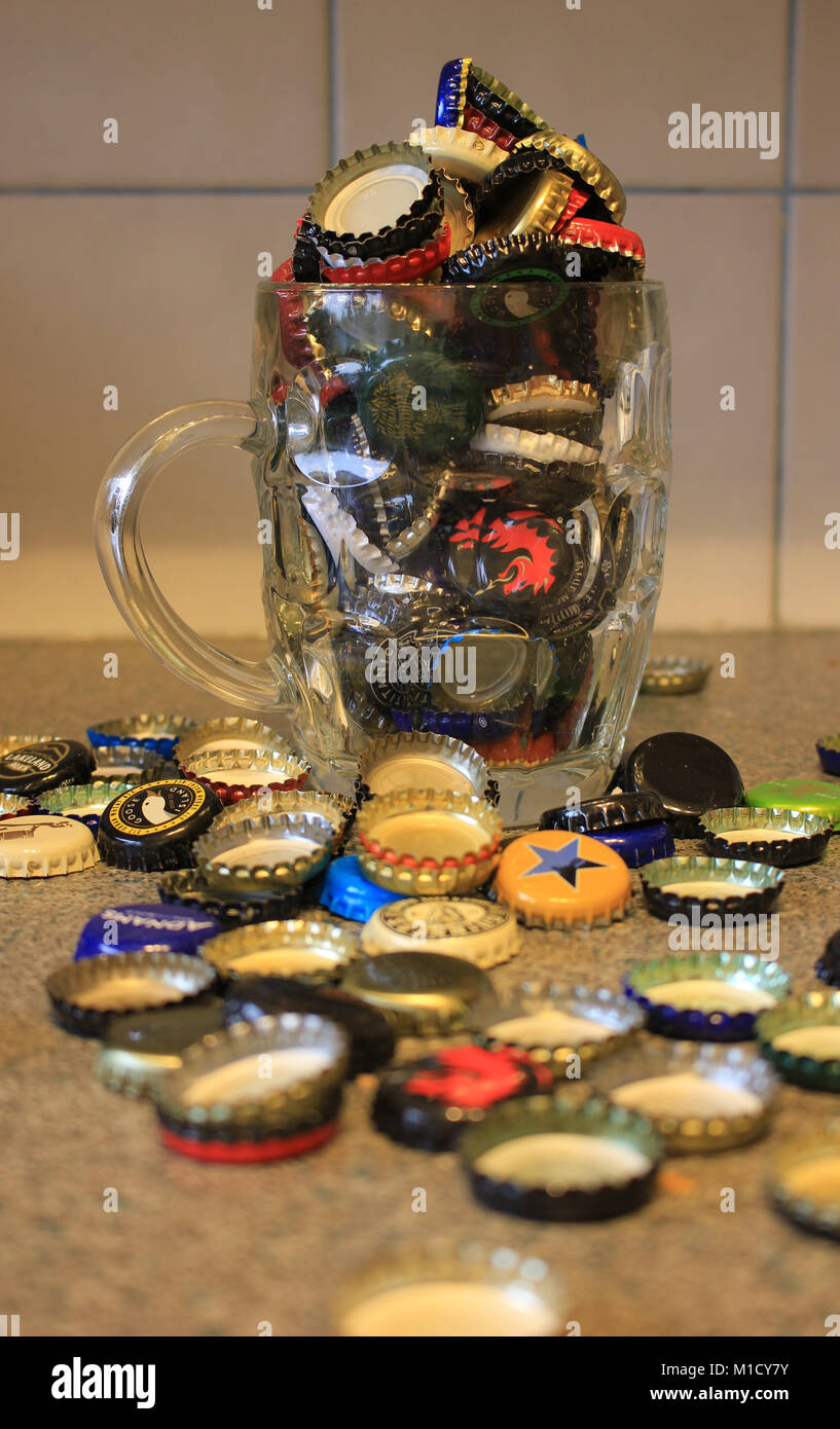 Used beer bottle tops collected after the beer has been drunk and are over flowing from a dimpled pint beer jug creating a colourful image. Stock Photo
