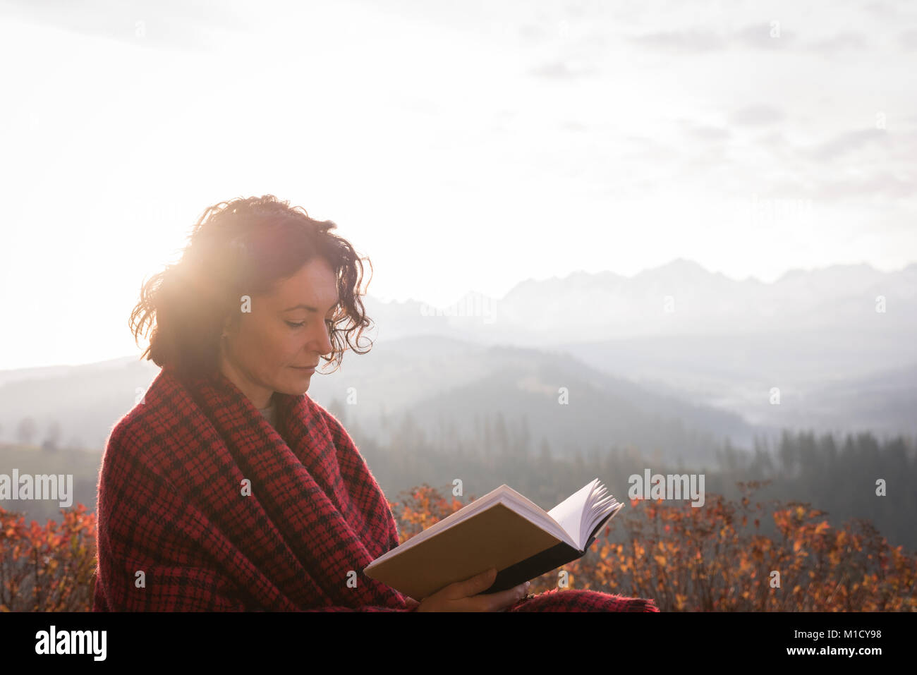 Beautiful woman wrapped in blanket reading book Stock Photo