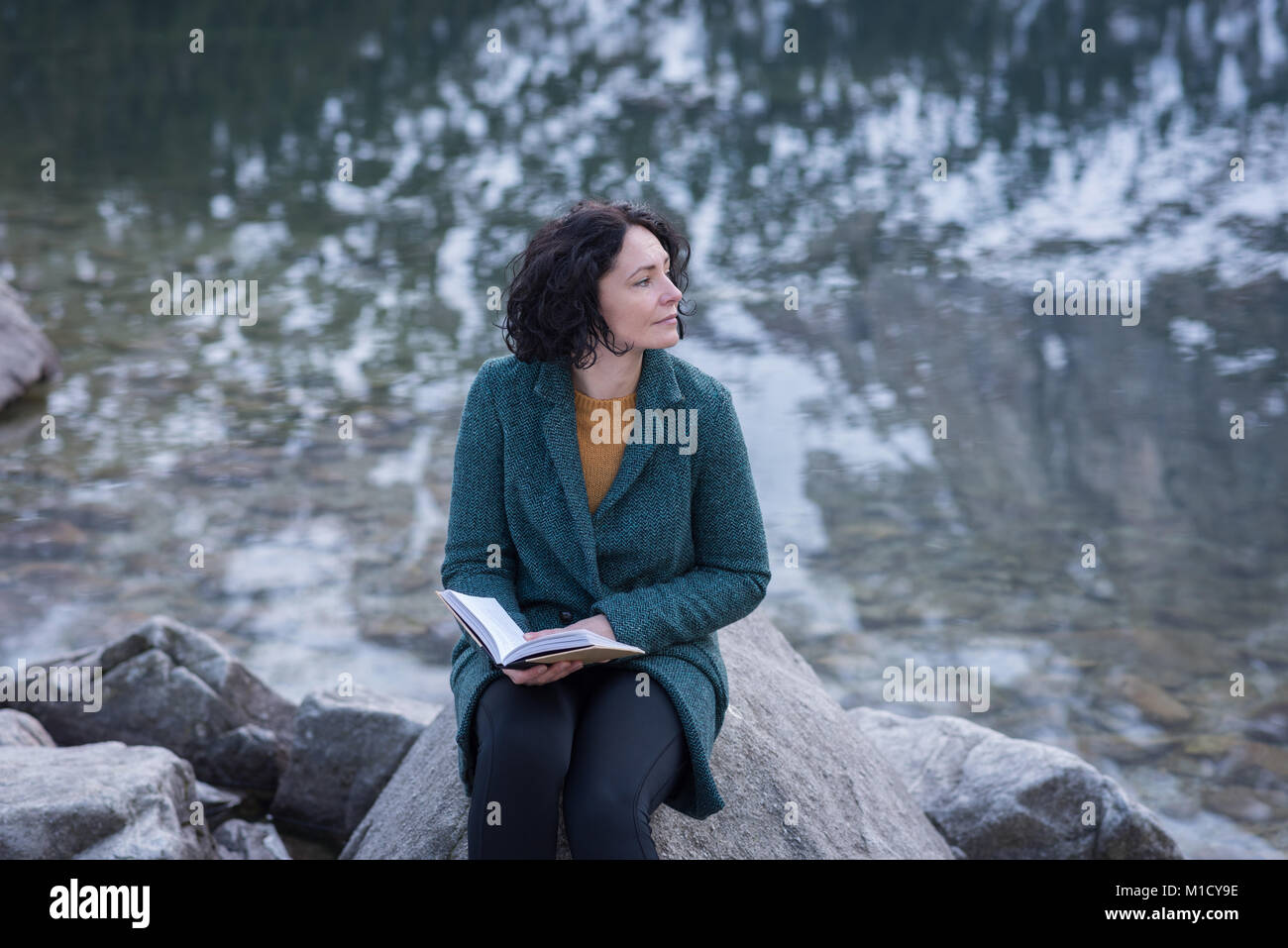 Thoughtful woman sitting with book at lakeside Stock Photo