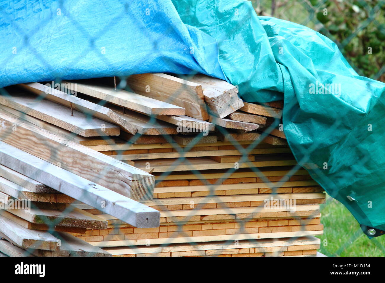 Construction site, piled wooden planks  under aqua blue tarpaulin. Stock Photo
