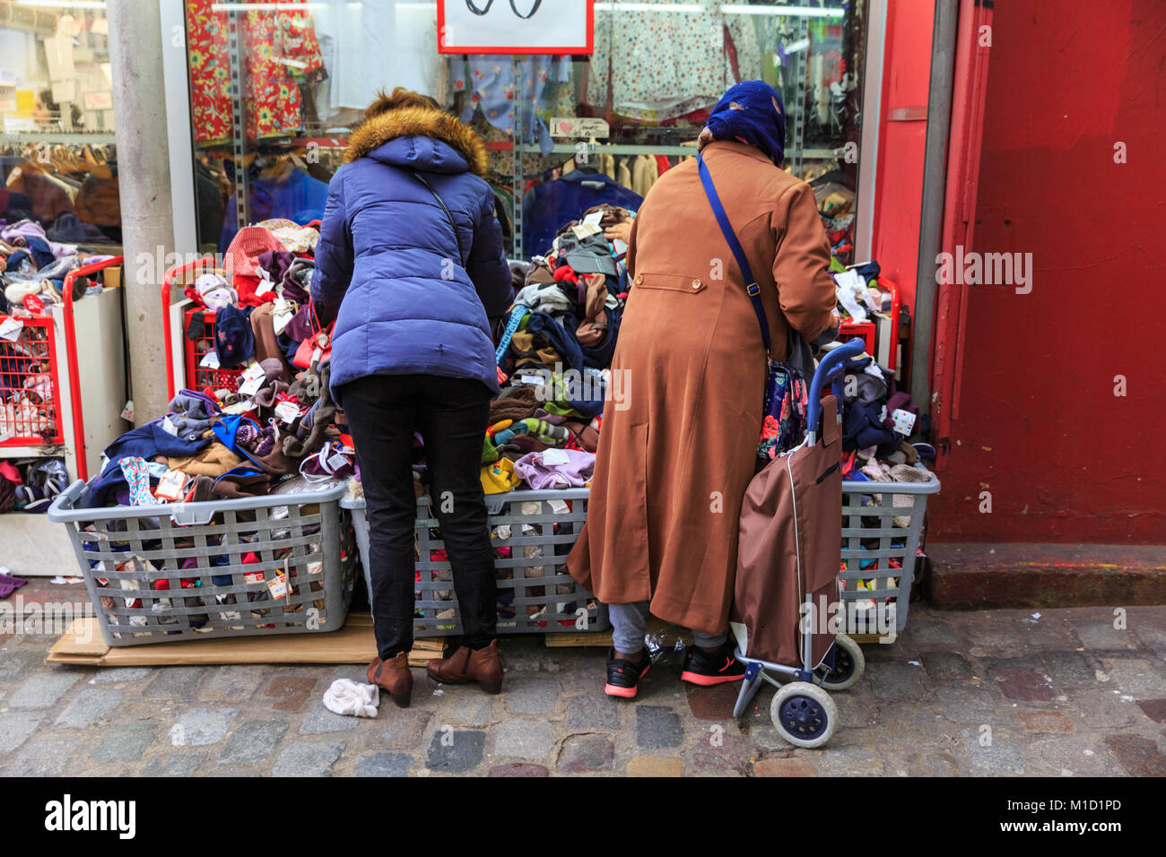 Bargain shopping, shoppers browse the heaps of cheap bargain clothes at shops and stalls in Quartier Pigalle, Paris, France Stock Photo