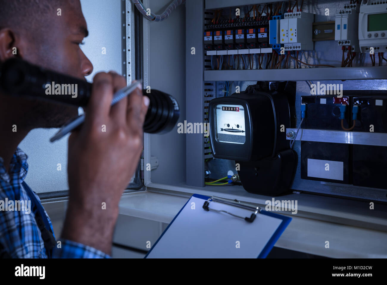 Close-up Of Male Technician Holding Flashlight And Clipboard In Front Of Fuse Box Stock Photo