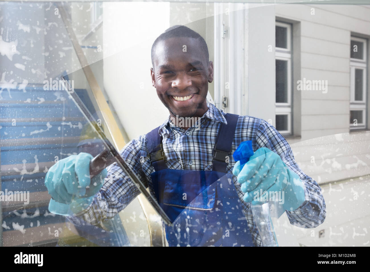 Happy Male Worker Cleaning Glass With Squeegee And Spray Bottle Stock