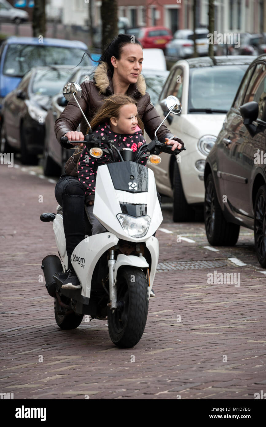 Under Dutch law it is not a requirement for anyone owing a motorbike or scooter under 30cc to wear a crash helmet.   A mother and daughter riding a sc Stock Photo