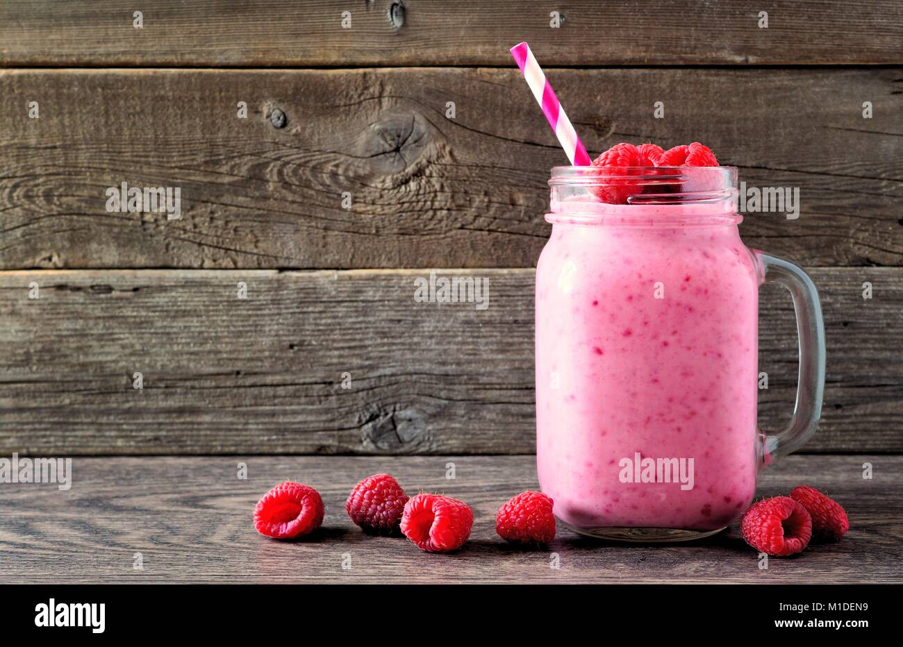 Raspberry smoothie in a mason jar glass with scattered berries over a rustic wood background Stock Photo