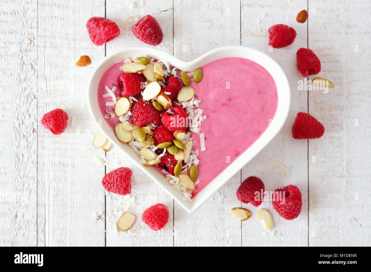 Healthy raspberry smoothie in a heart shaped bowl with superfoods. Above scene on a white wood background. Stock Photo