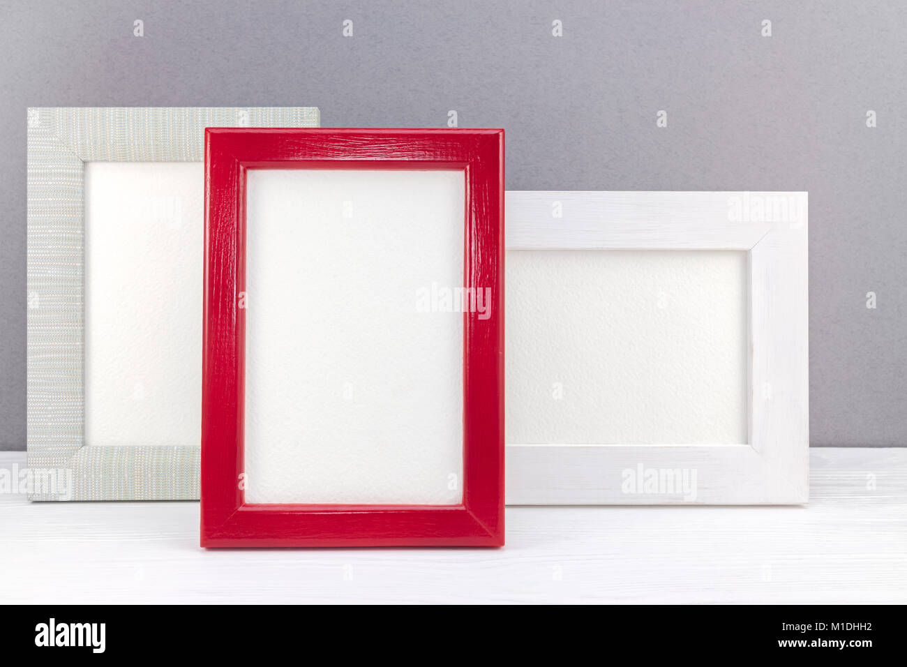 different empty photo frames on white wooden desk against grey wall background Stock Photo