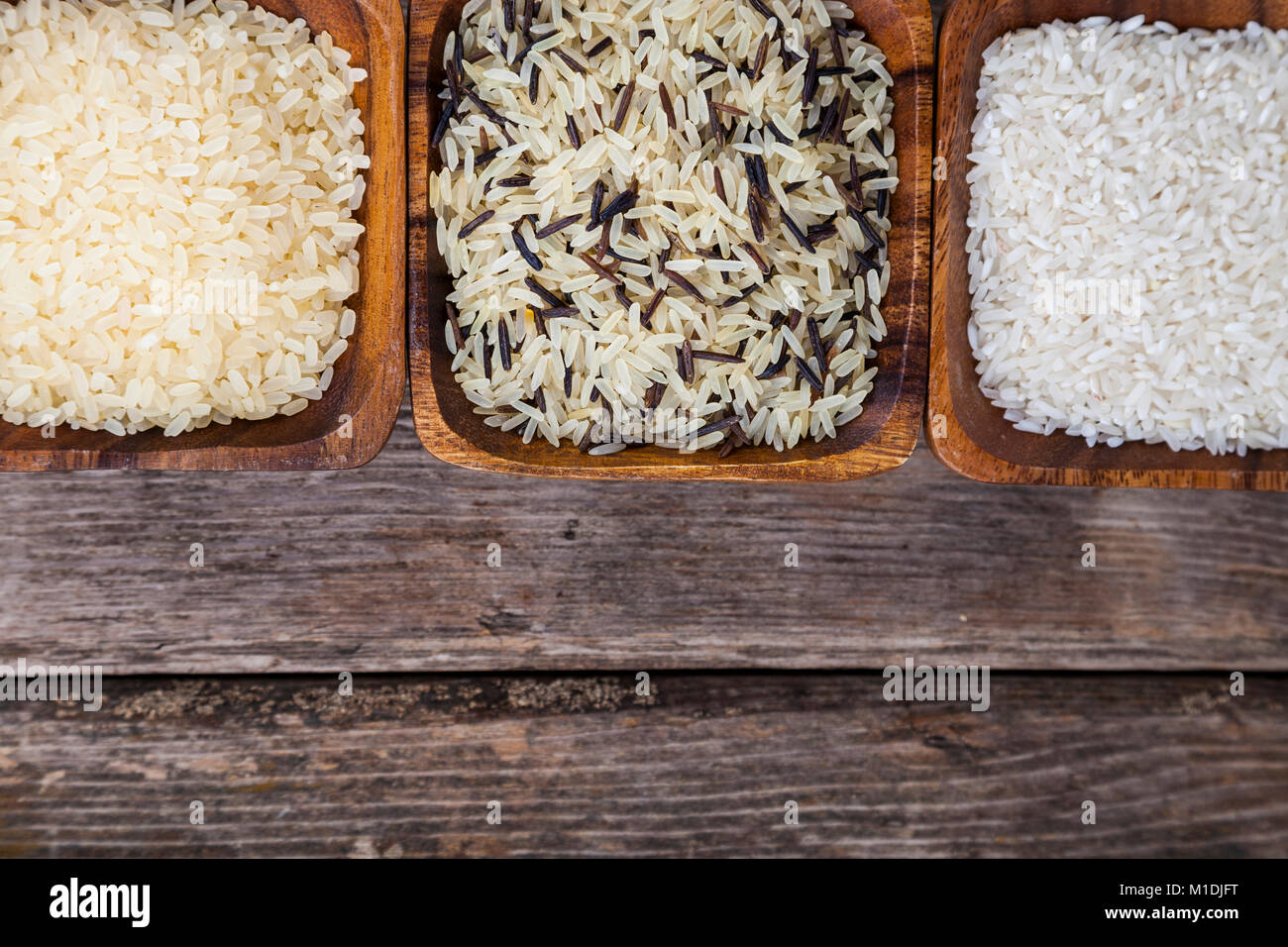 Three bowls with different varieties of rice on a wooden background