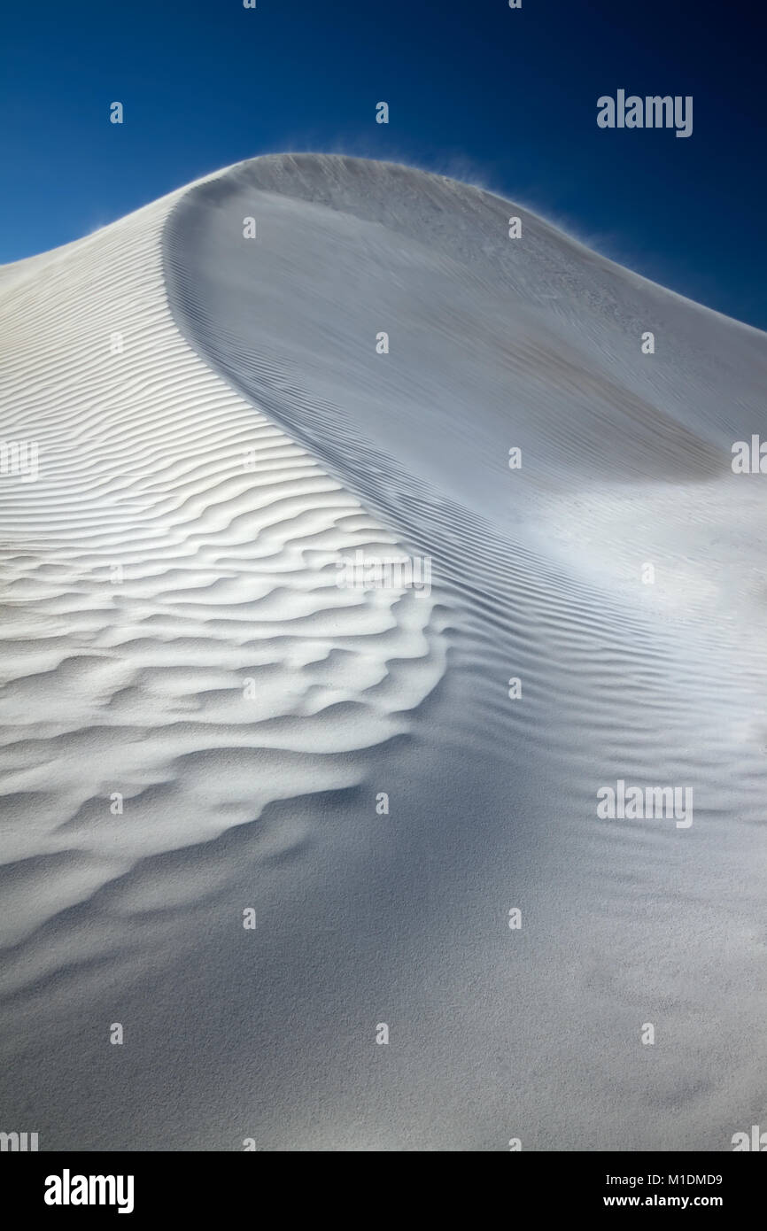 A white sand hill with ripples on the exposed side and smoother sand on the protected side. There are thin wisps of sand on the crest of the hill Stock Photo