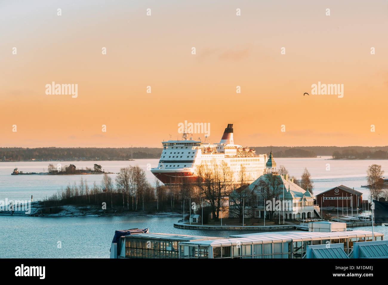 Helsinki, Finland. View Of Modern Ferry Ferryboat Sailing Near Blekholmen Valkosaari Island On Background Of Sunset Sunrise Sky. Stock Photo