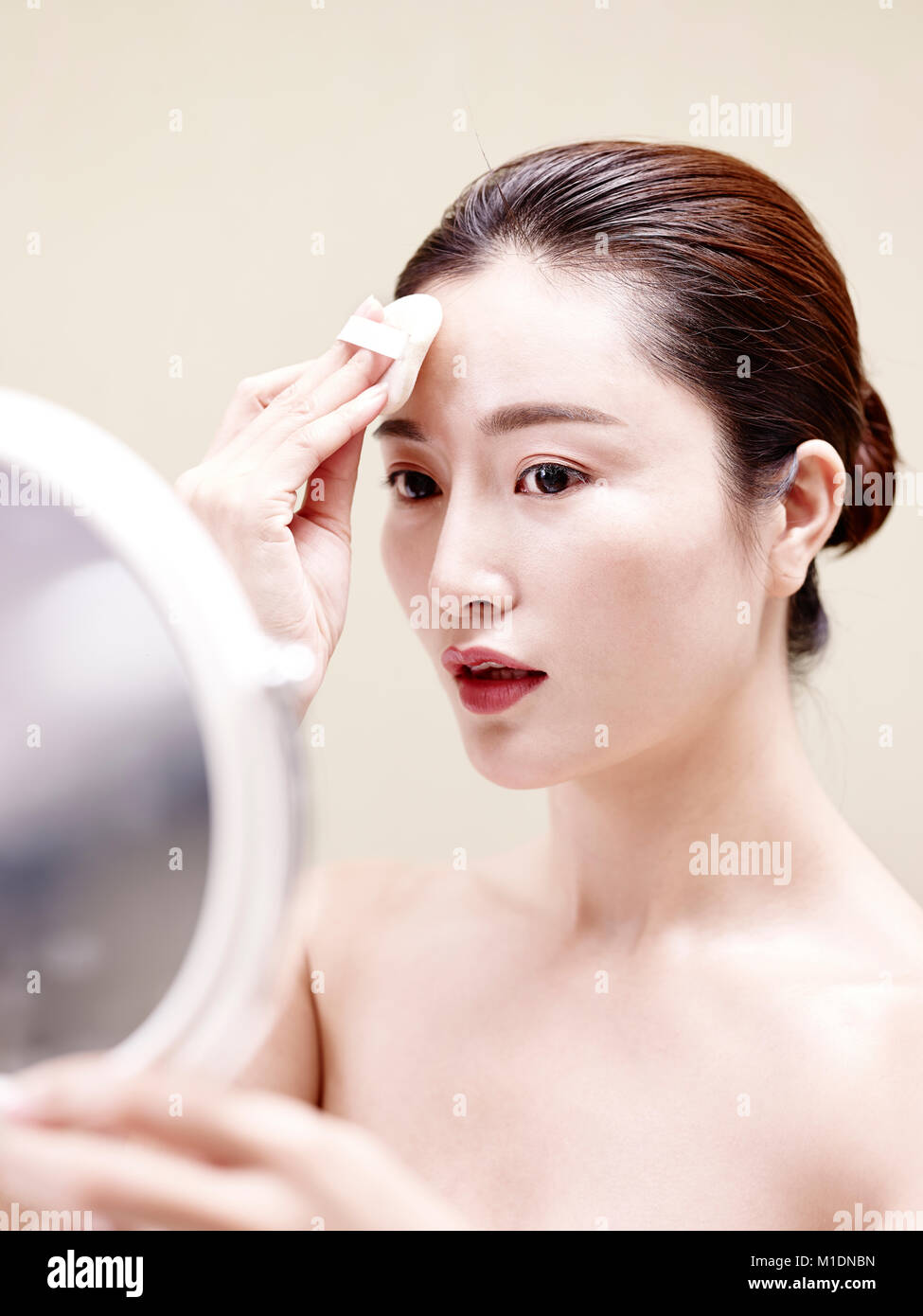 beautiful young asian woman looking in the mirror while cleansing face with a sponge Stock Photo