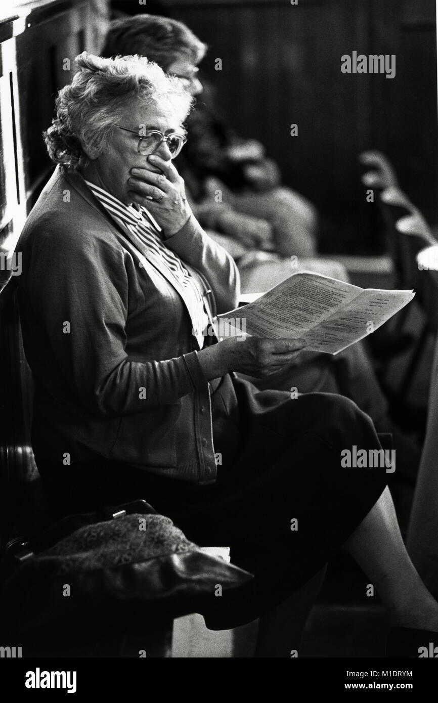 Elderly lady in audience reading the programme at small eisteddfod in village hall at Trefeglwys Powys Wales UK Stock Photo