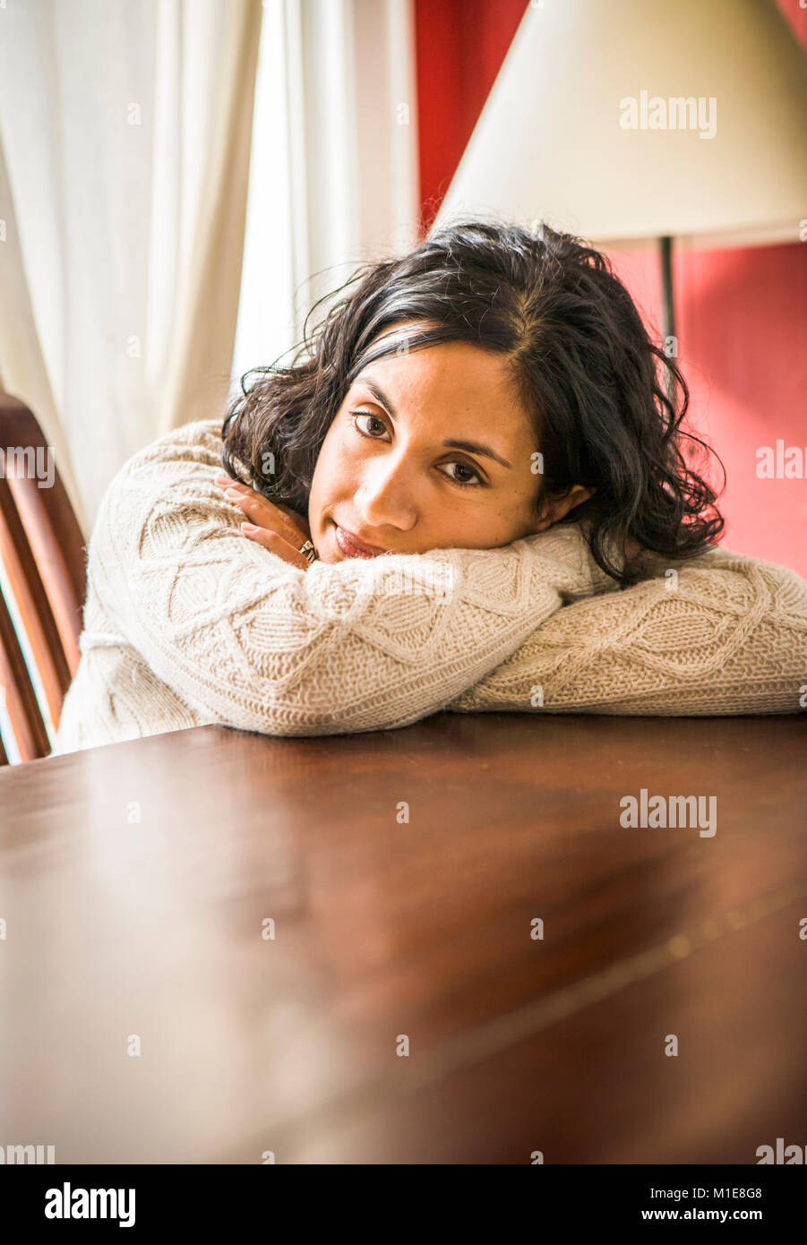 A portrait of an early 30's Sri Lanken - American woman leaning on a table and resting her head on her arms. Stock Photo