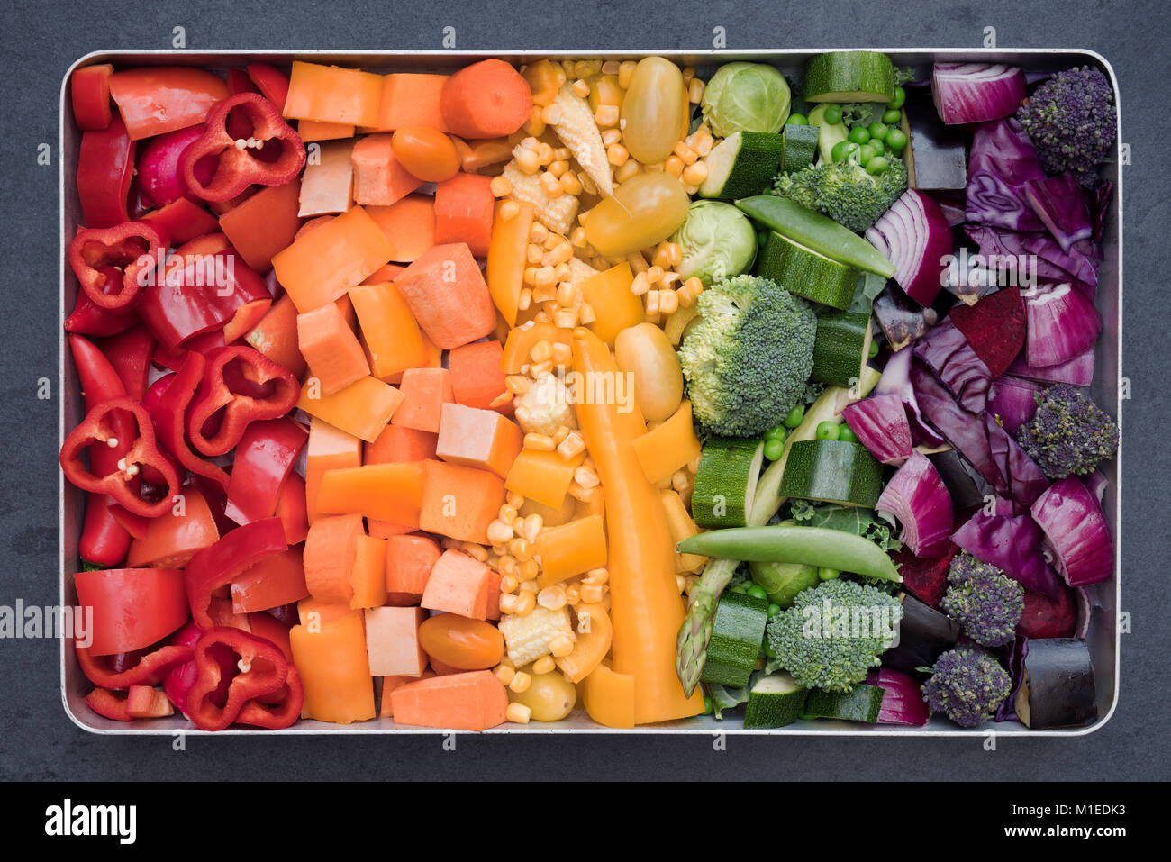 Cut Colourful Vegetables in a baking tray on a slate background Stock Photo