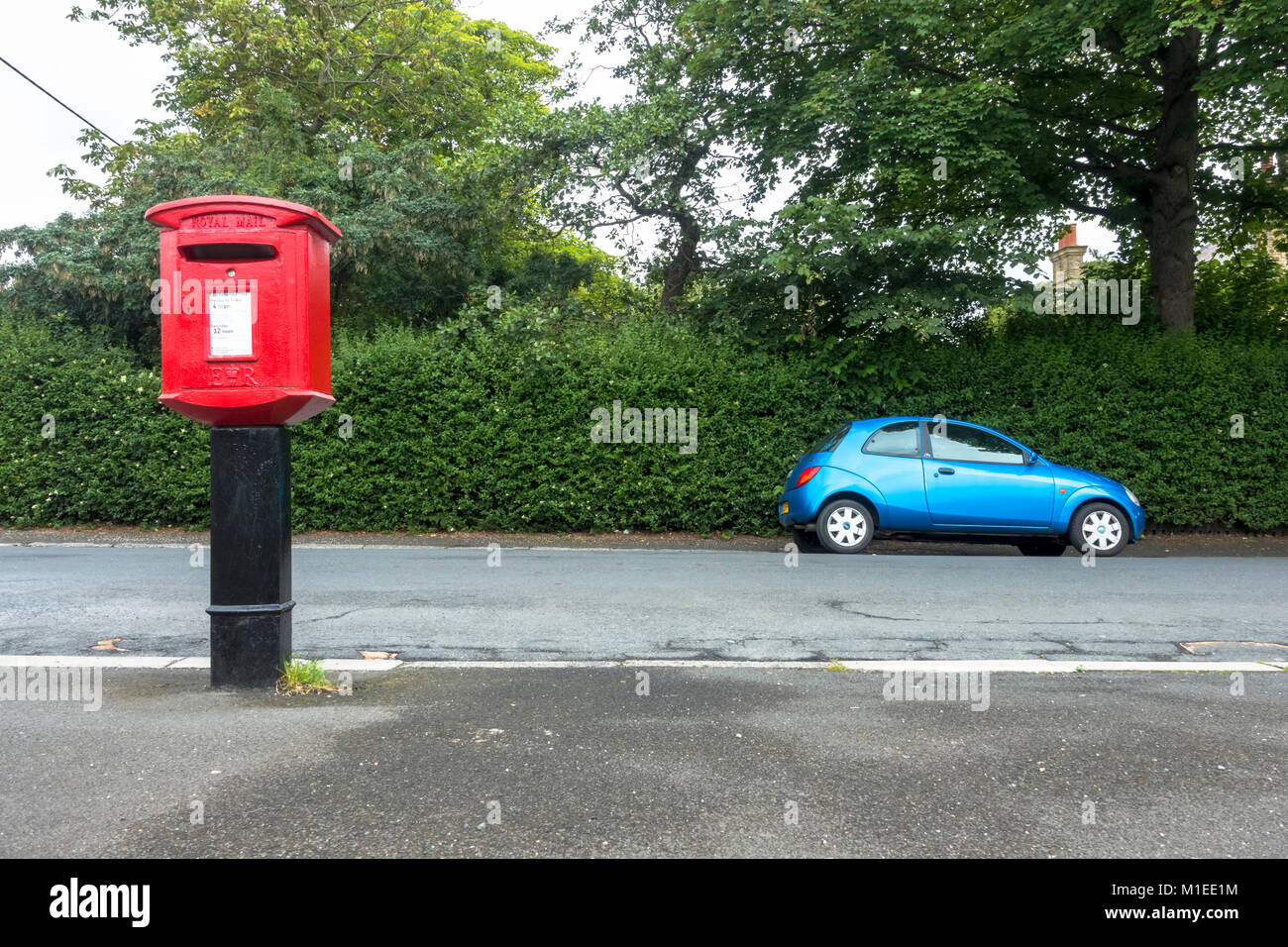 A small blue car opposite a red post box, uk Stock Photo