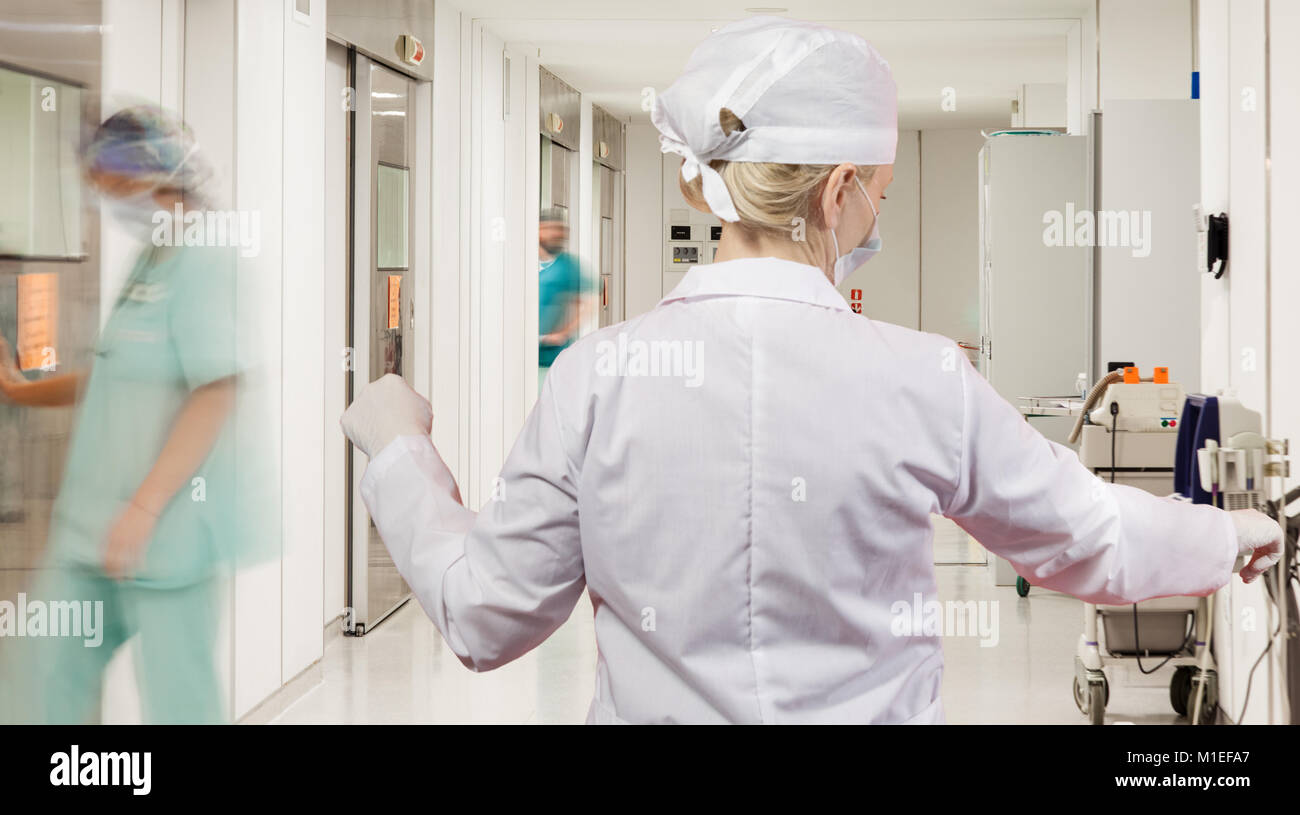 A sterile corridor to operating rooms in modern hospital with female doctor over motion blurred figures of doctors and nurses. Stock Photo