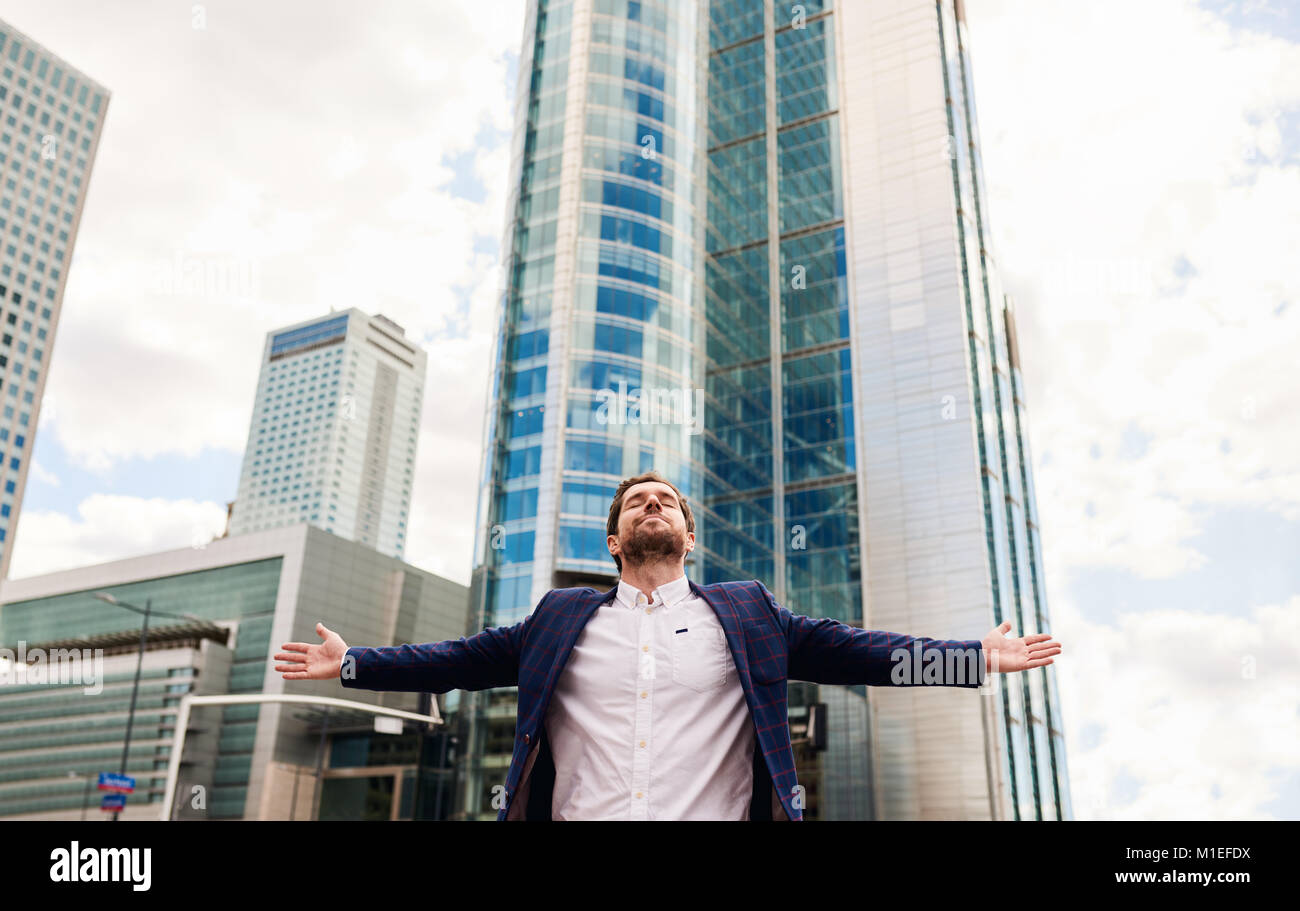 Businessman standing with arms raised skyward in the city Stock Photo
