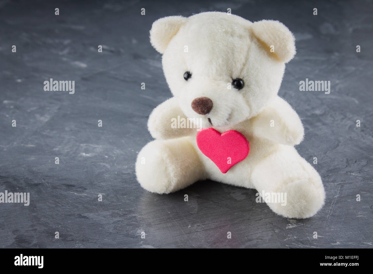 White toy teddy bear with heart on a gray background. The symbol of the ...