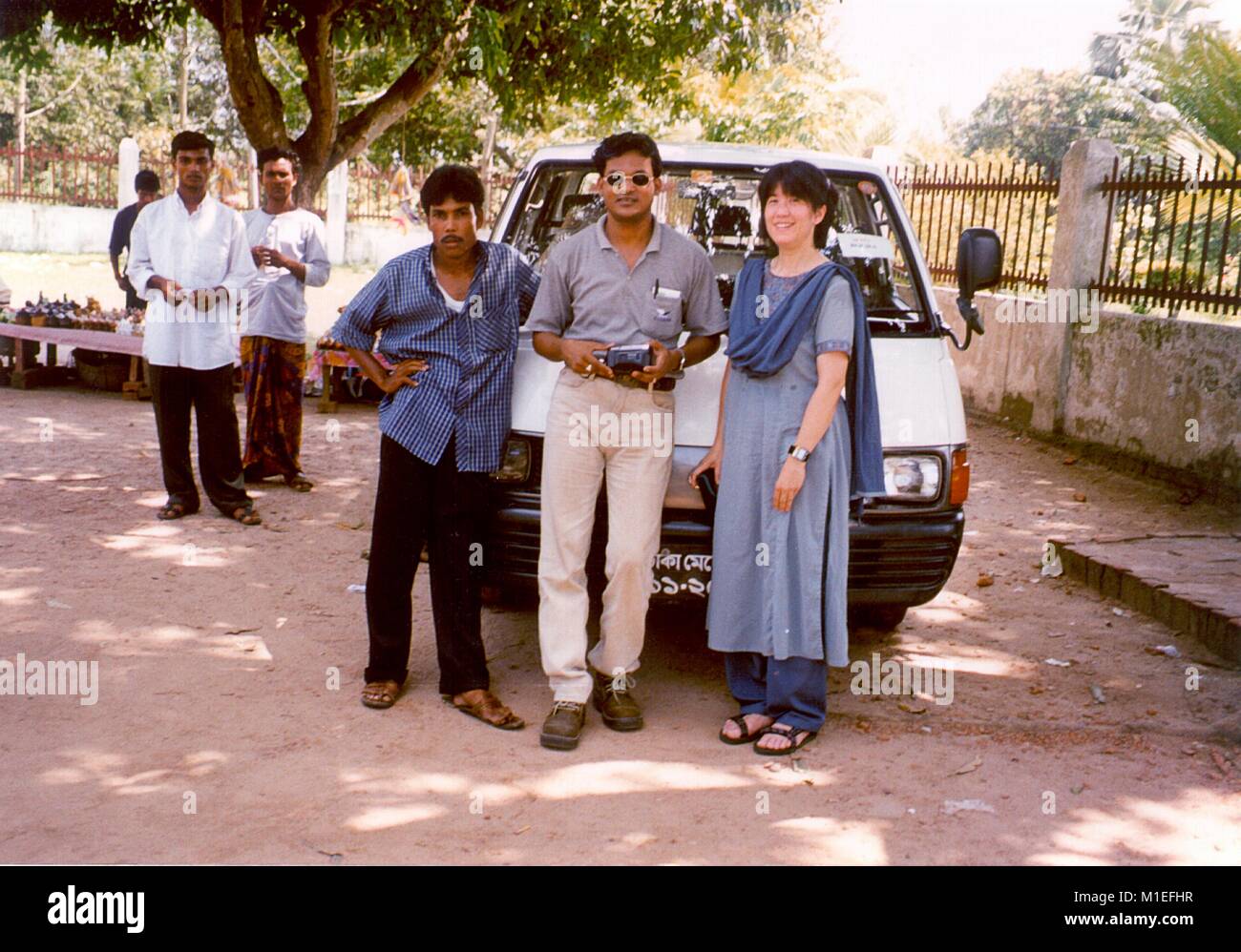 Photograph of Dr. Badrul Munir Sohel (WHO) and Dr. Pamela Ching (CDC) posing in front of a van among locals in a rural area in the Rajshahi Division of Bangladesh, during a surveillance stage of AFP (Acute Flaccid Paralysis) cases identification in children, as part of the global resolution to eradicate polio, image courtesy CDC/Dr. Pamela Ching, 1999. () Stock Photo
