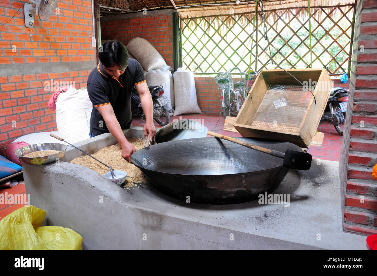 February 18, 2015.  Vinh Long, Vietnam.  A Vietnamese man in Vinh Long, South Vietnam lighting a fire under a large metal wok to make toasted rice can Stock Photo
