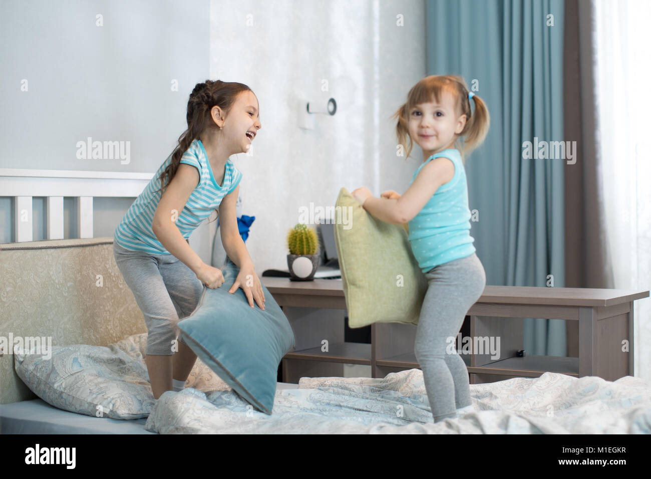happy kids sisters having a pillow fight in bed at home Stock Photo