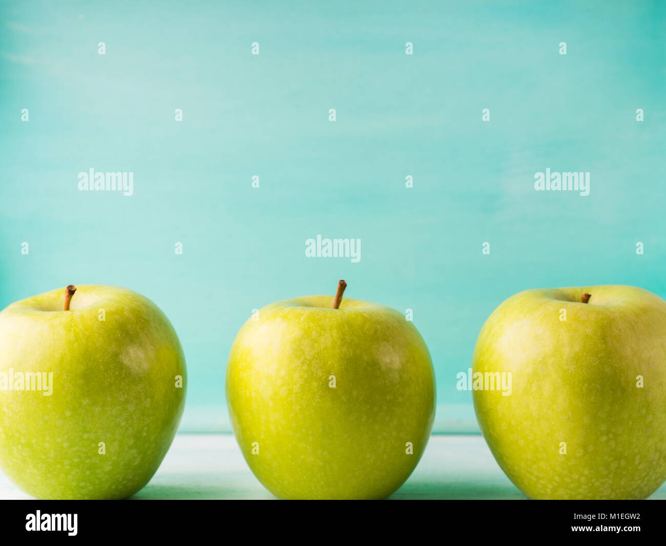 Three Green apples on turquoise background. Healthy food three pillars
