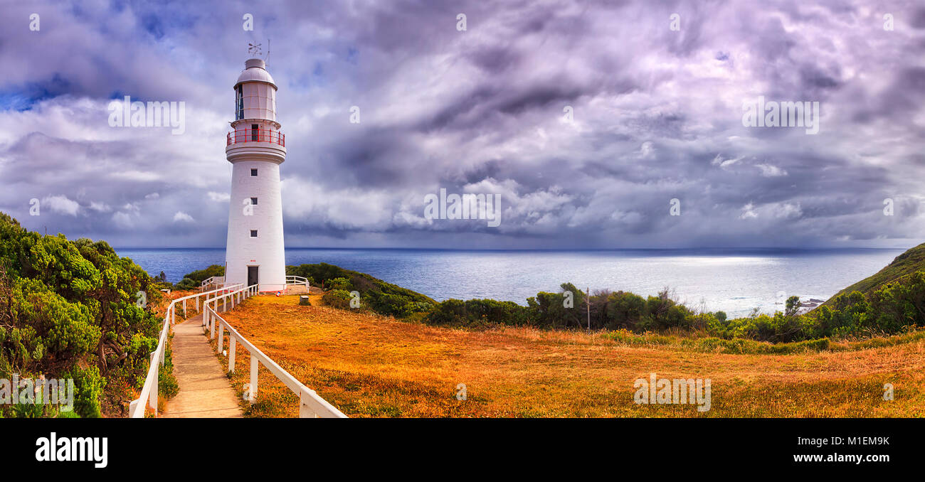 Remote historic white lighthouse on Cape Otway elevated cliff overlooking distant and isolated seas of southern ocean agaisnt clody and moody sky. Stock Photo