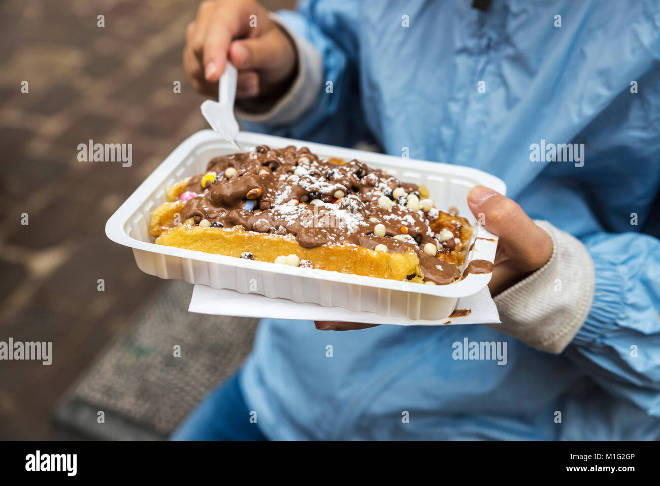Little girl eating a waffle of chocolate on a street in the medieval city of Bruges, Belgium Stock Photo