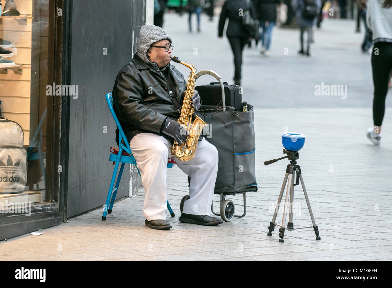 A street busker playing his saxophone hoping for cash donations on the streets of Liverpool city centre, United Kingdom Stock Photo