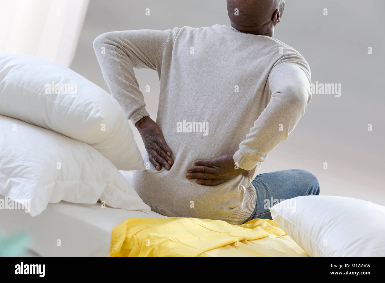 African American man with severe backache sitting on bed in his bedroom Stock Photo
