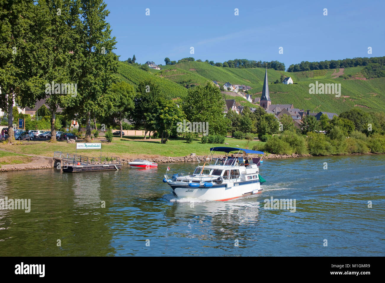 Motor boat cruising on Moselle river, behind the church Saint Maternus of wine village Uerzig, Moselle river, Rhineland-Palatinate, Germany, Europe Stock Photo