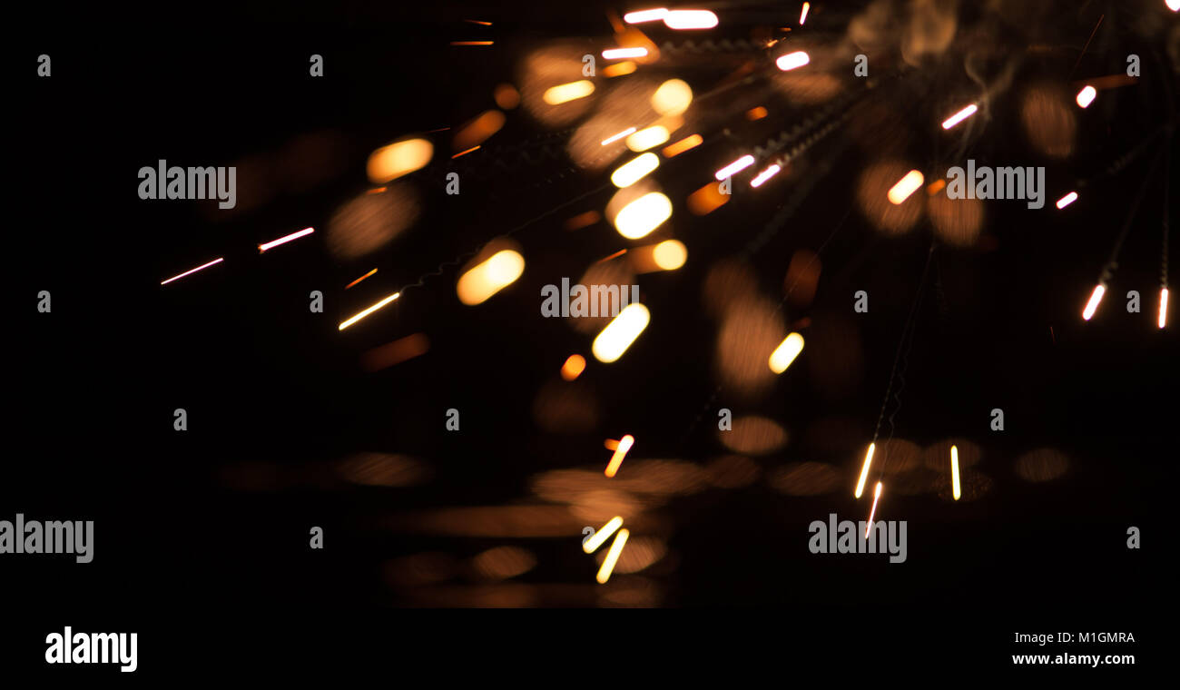 A long exposure macro shot showing fragments of burning magnesium falling onto a black reflective surface. Stock Photo