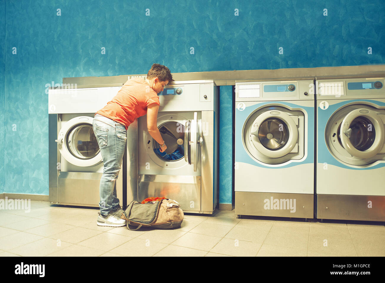 A girl fills up a public automatic washing machines with dirty cloths. Stock Photo