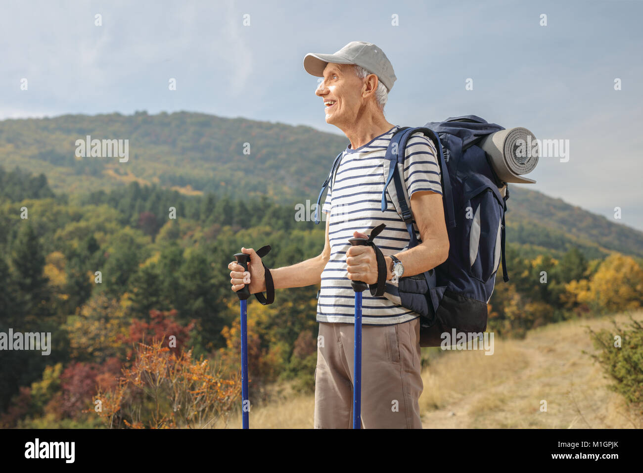 Elderly hiker with hiking poles and a backpack looking away outdoors Stock Photo