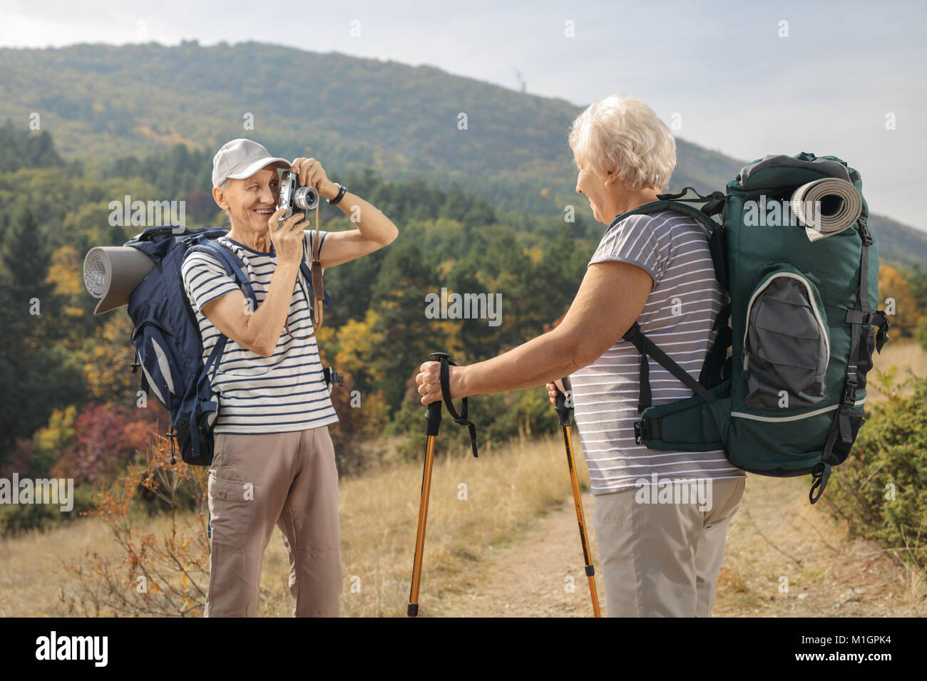 Elderly male hiker taking a picture of an elderly female hiker outdoors Stock Photo