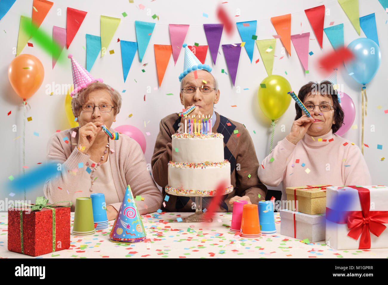 Seniors celebrating a birthday with a cake and party horns Stock Photo
