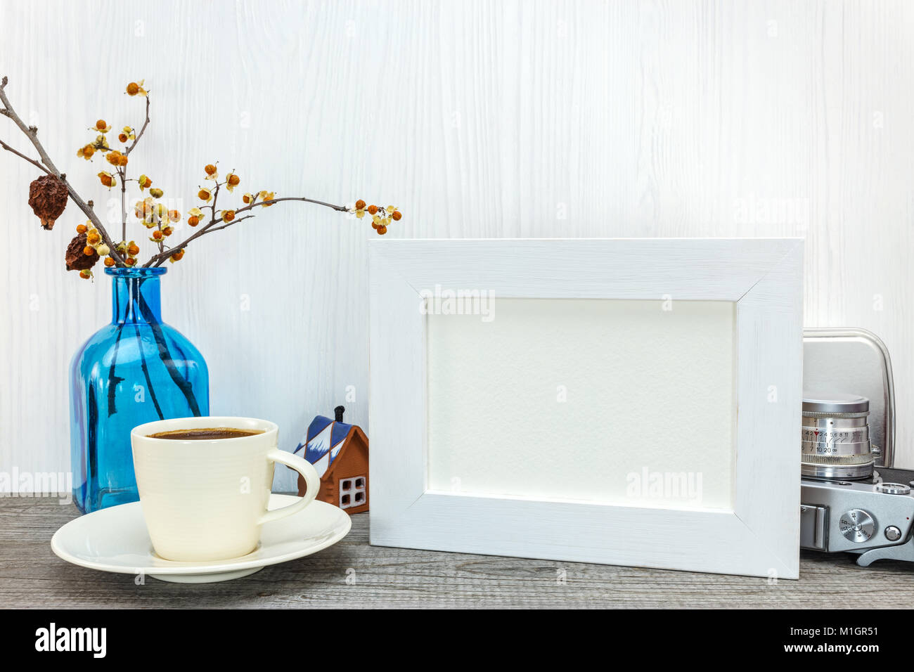 empty white photo frame, cup of coffee, blue glass vase with dried